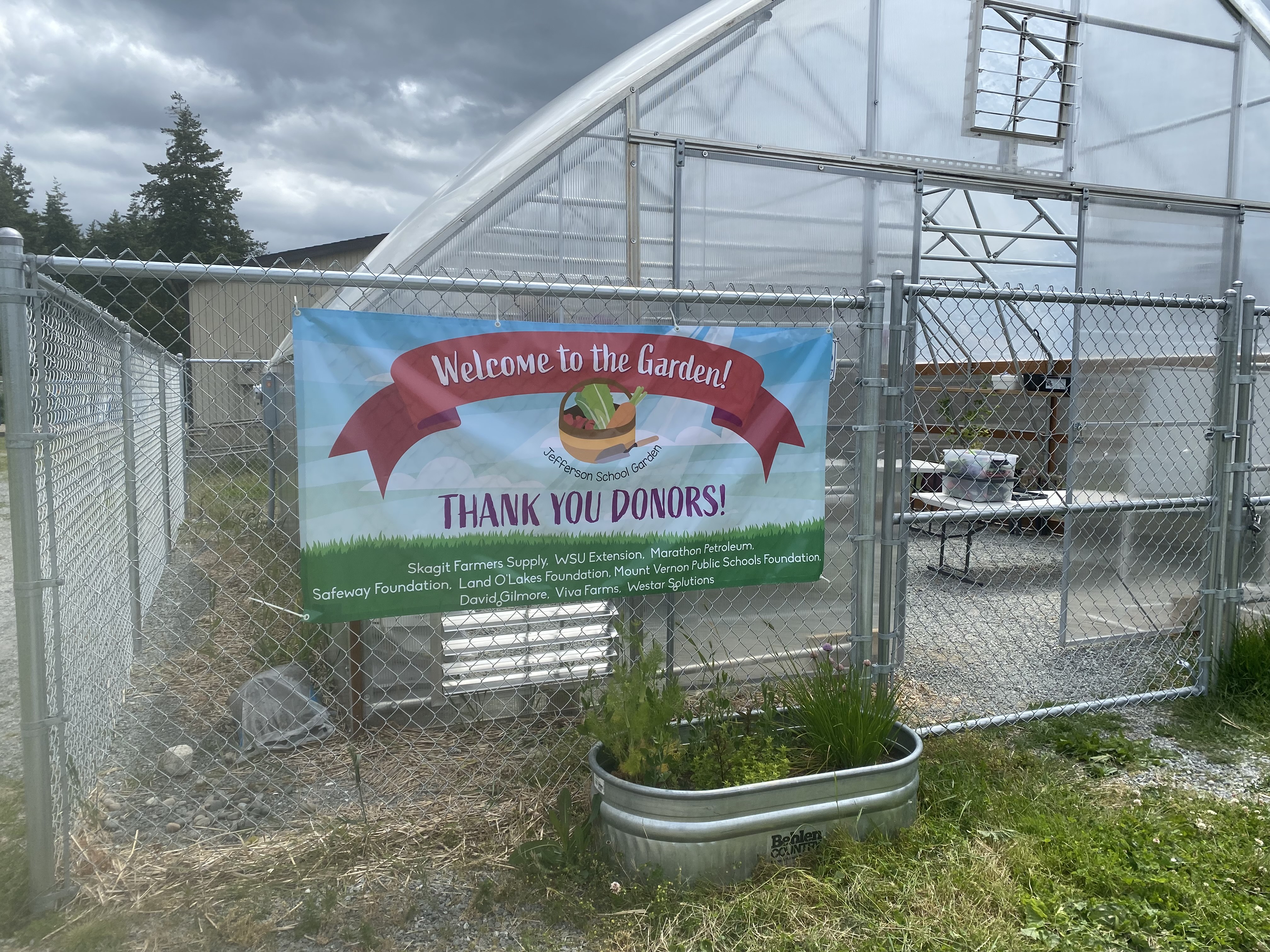 Picture of a greenhouse with banner hung on the fence thanking all the donors.